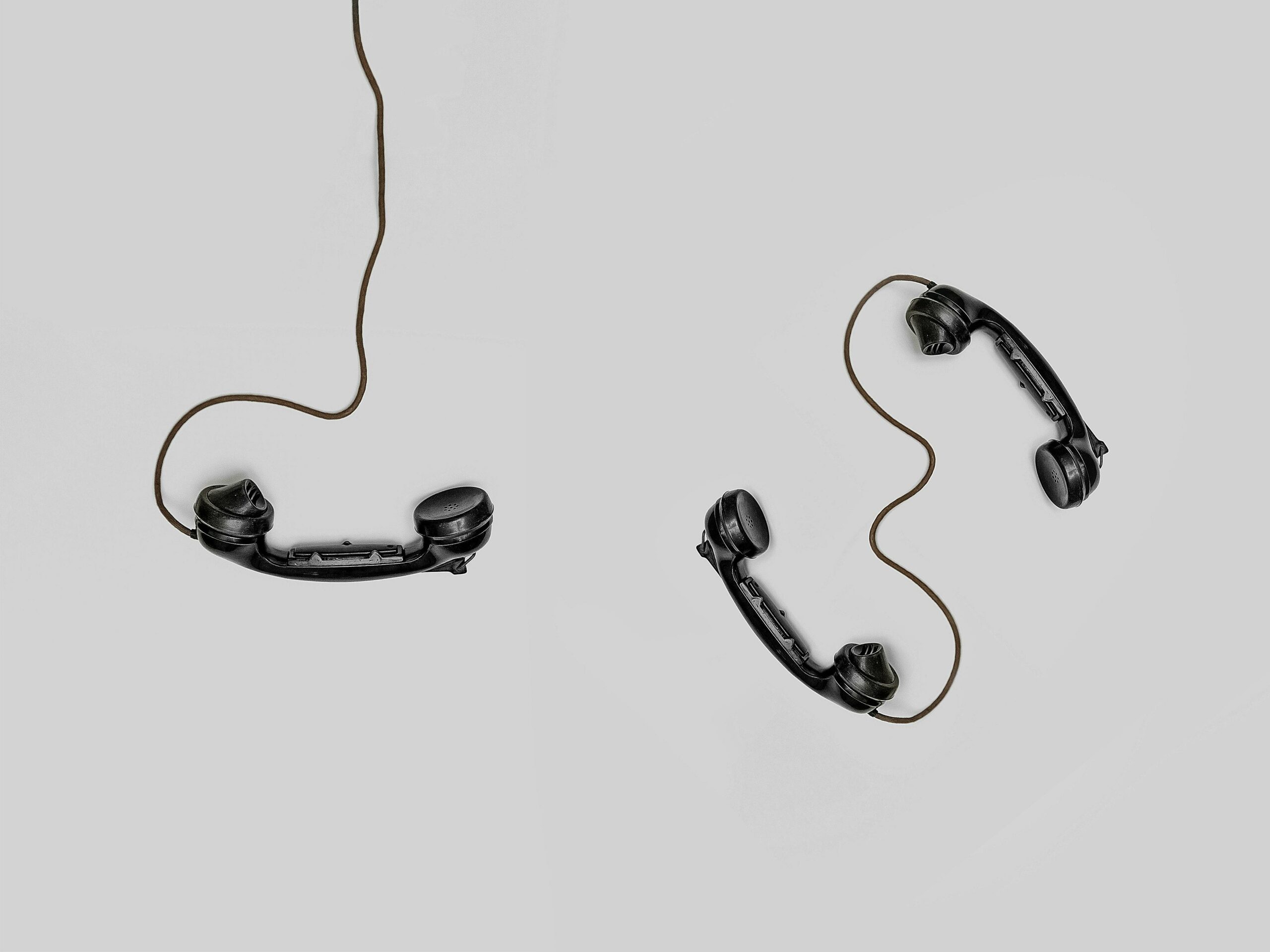 Schwarze Telefonhörer mit Kabel auf weißem Untergrund.